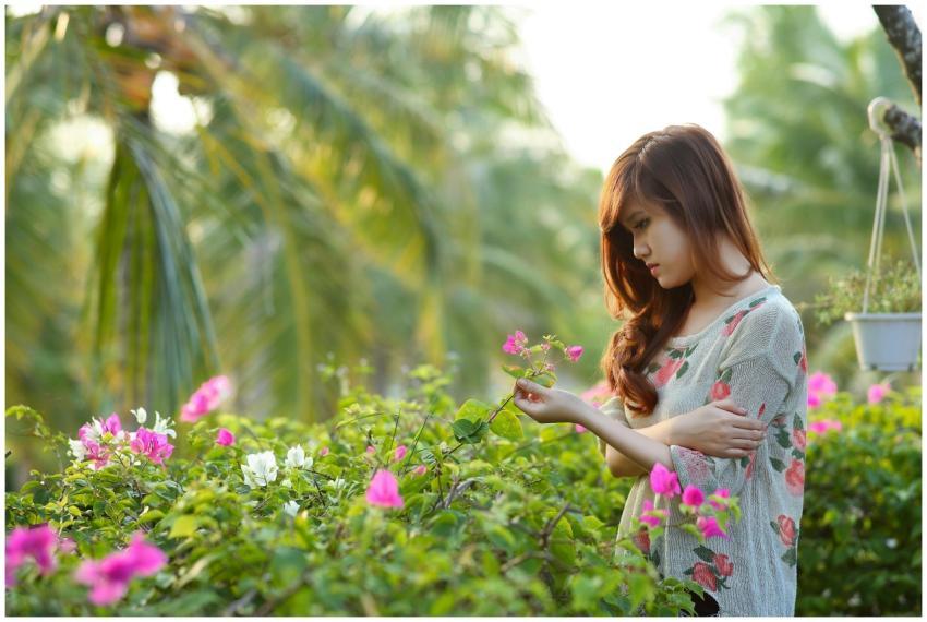 Pensive young woman holding a flower, surrounded b