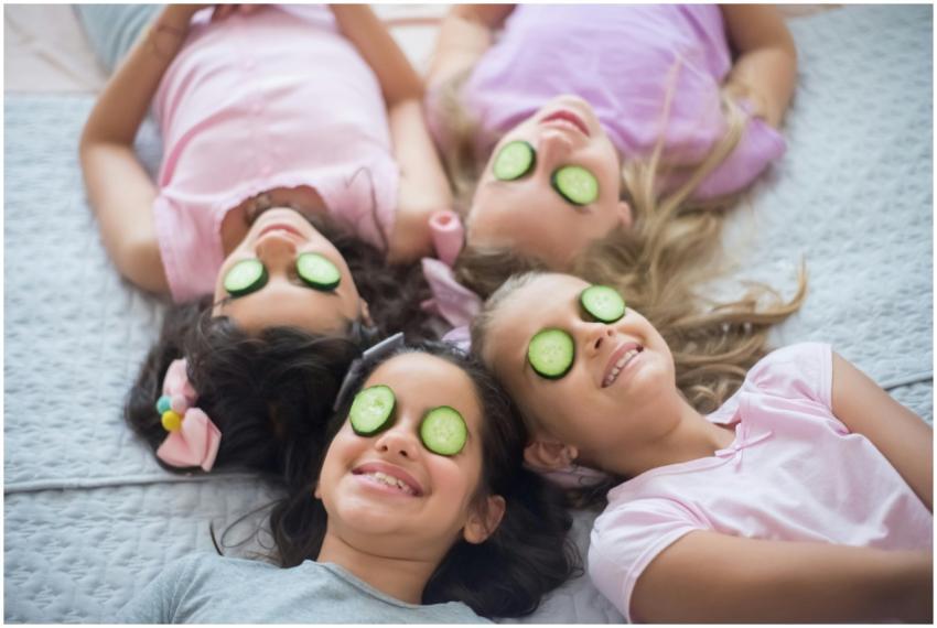 Four girls lying on a bed with cucumber slices on