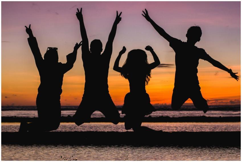 Silhouette of friends jumping on the beach at suns