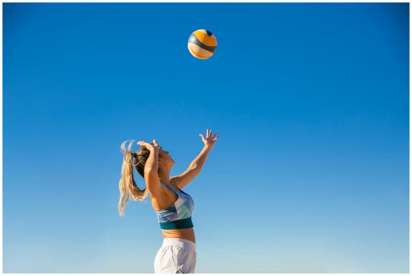A woman spiking a volleyball on the beach under a