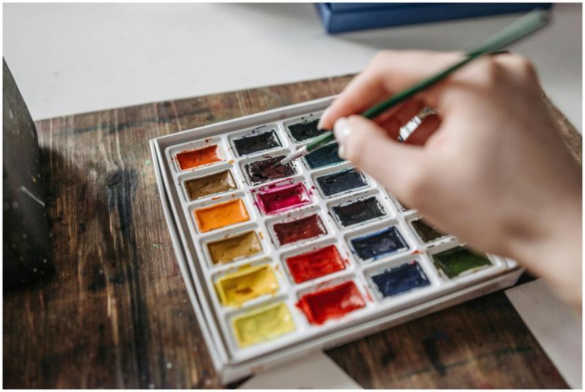 An artist's hand selecting a watercolor from a vib