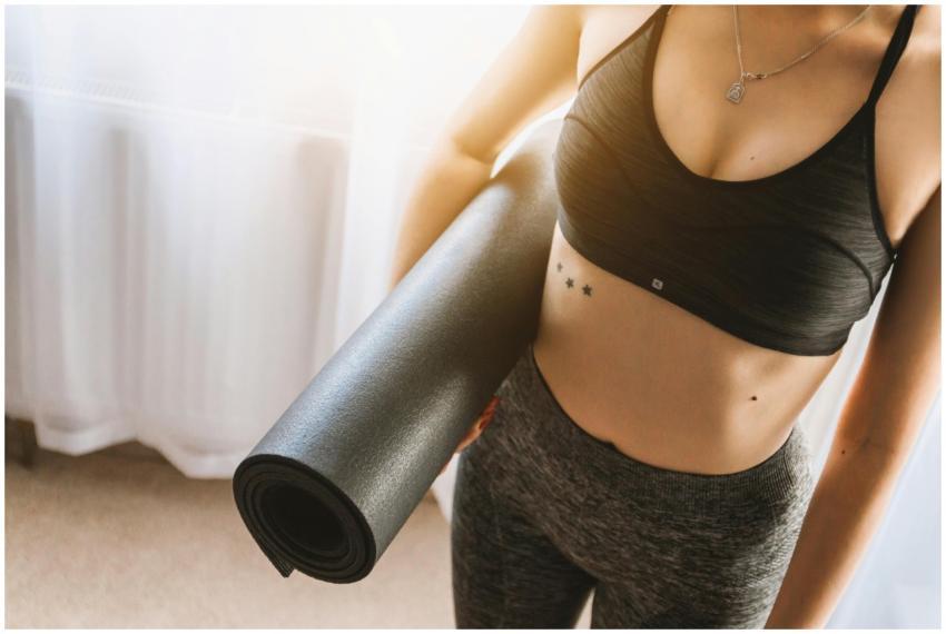 Fit woman in active wear holding yoga mat indoors,