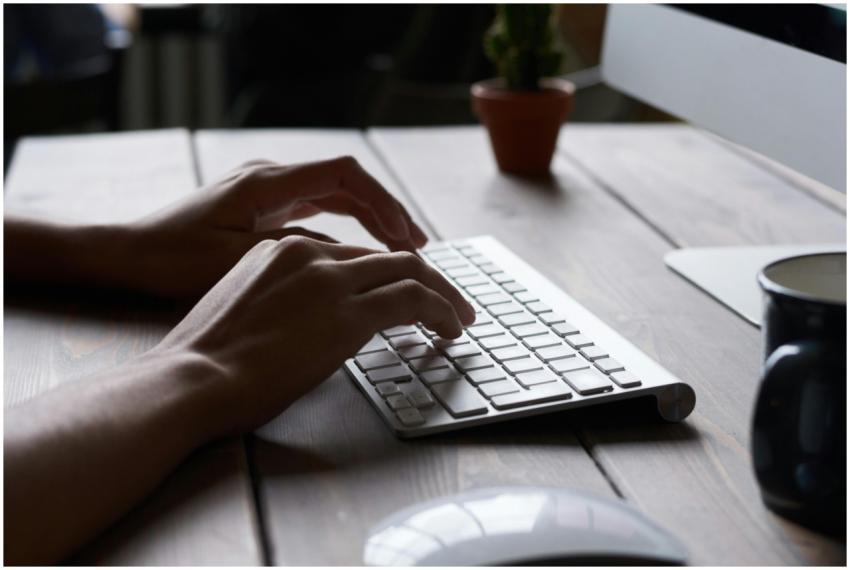 Close-up of hands typing on a wireless keyboard at