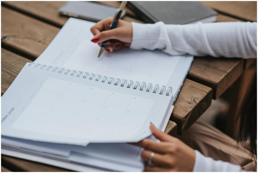 A woman writes in a planner at an outdoor wooden t