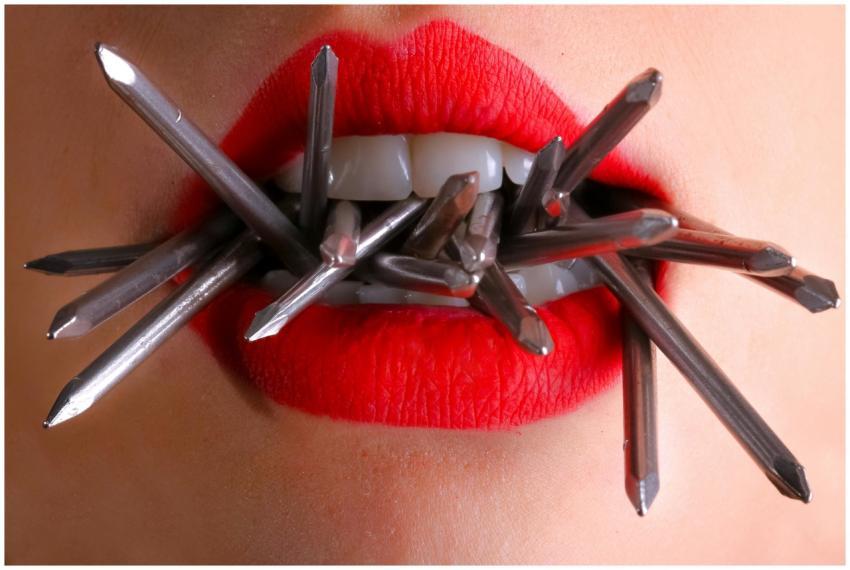 Artistic close-up of red lips biting metal spikes,