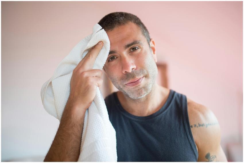 A man wipes sweat with a towel indoors, showcasing