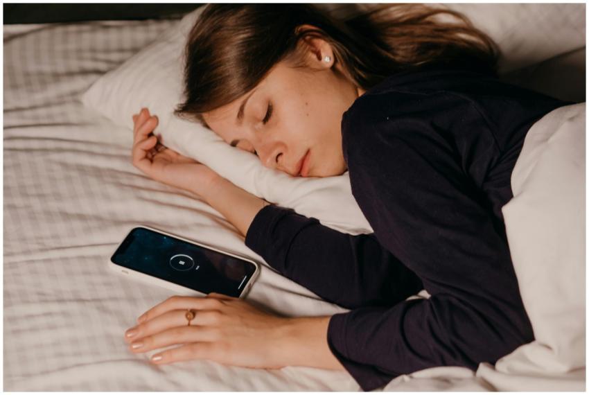 A woman peacefully sleeping in bed with a smartpho