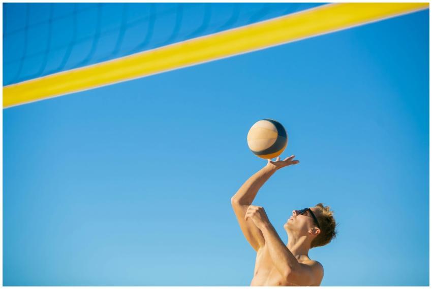 A man in sunglasses serves a volleyball outdoors o