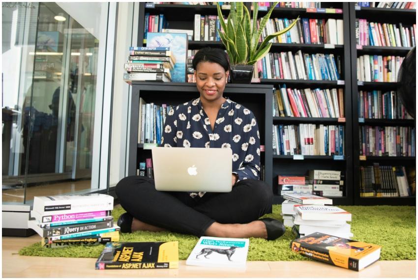 A woman sitting on a carpet in a library working o