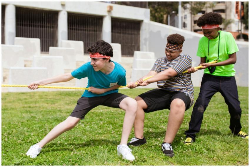 Group of boys playing tug of war on green grass du