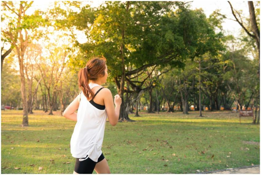 A woman jogging through a forest park in the early