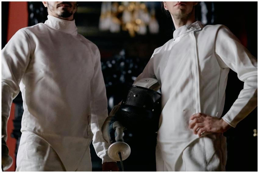 Two fencers in full gear pose confidently indoors,