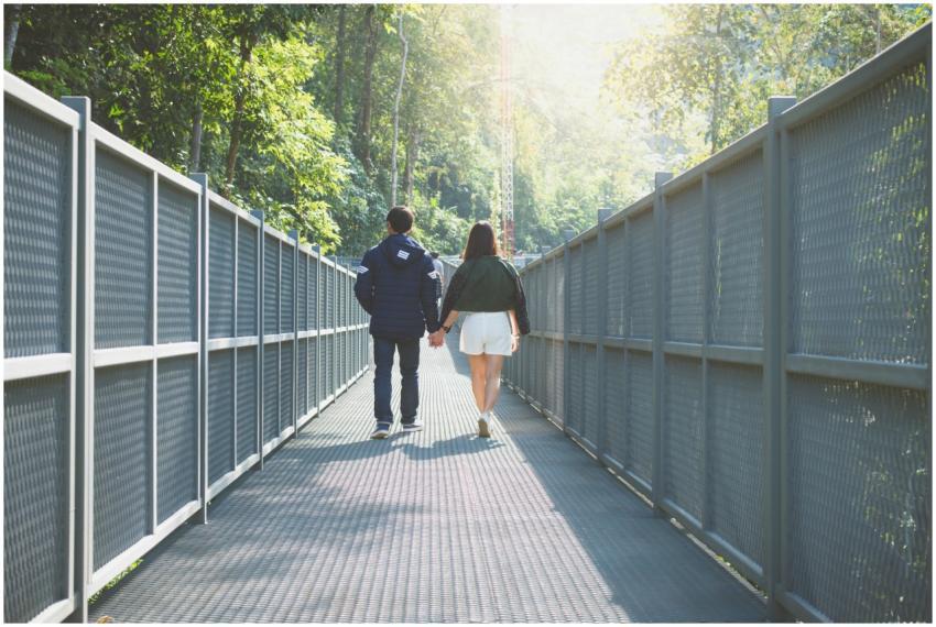 A couple holding hands walking along a forest brid