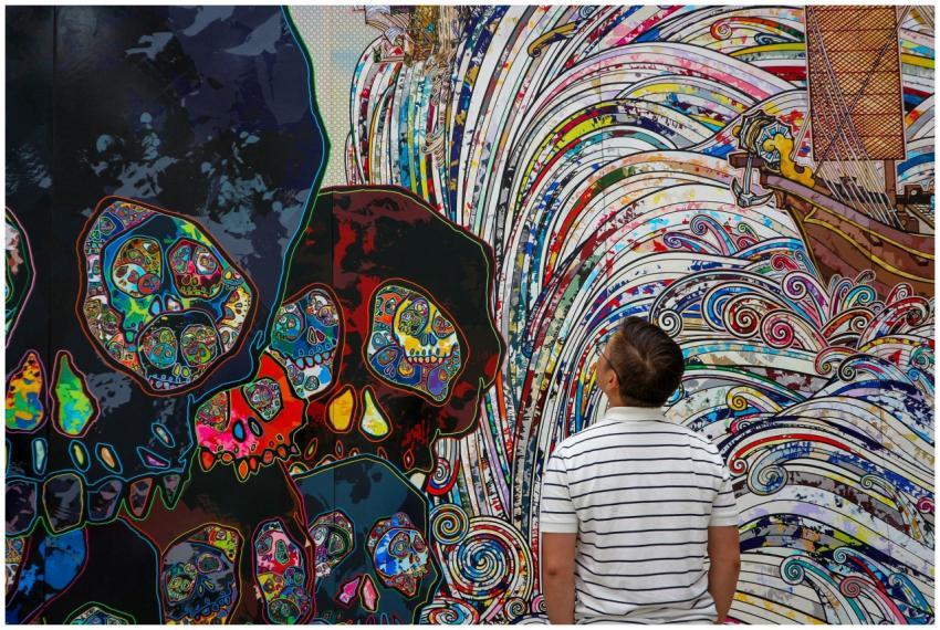 A man in a striped shirt views a colorful mural wi