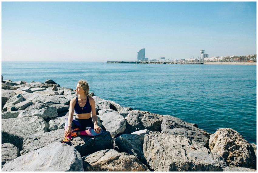 A woman in activewear meditates on rocky shore wit