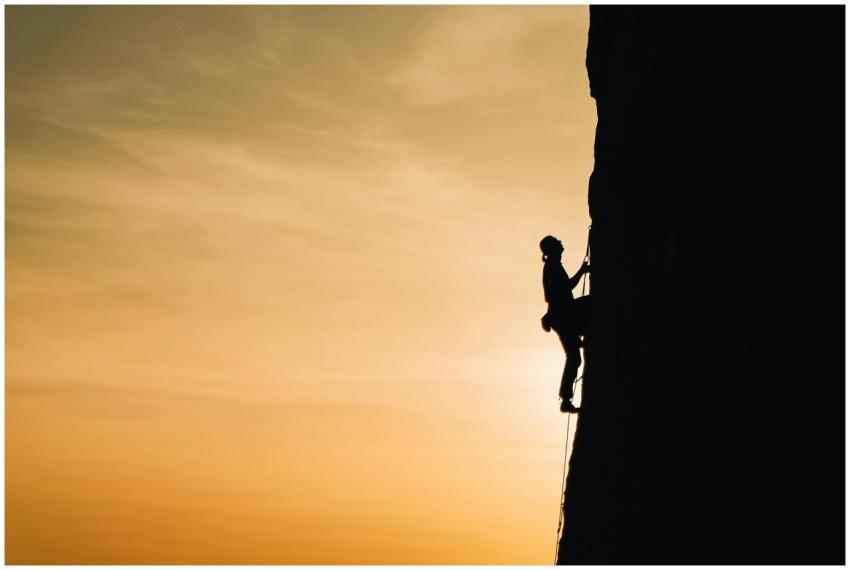 A silhouette of a rock climber scaling a steep cli