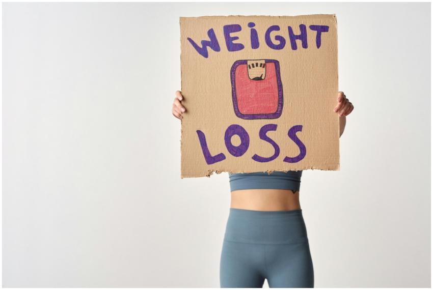 Person holding 'weight loss' sign for fitness moti