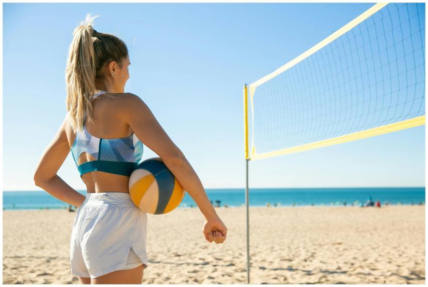 A woman holding a volleyball stands by a net on a