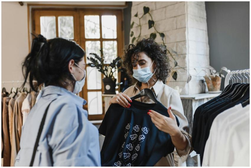 Two women wearing face masks shop for clothes in a