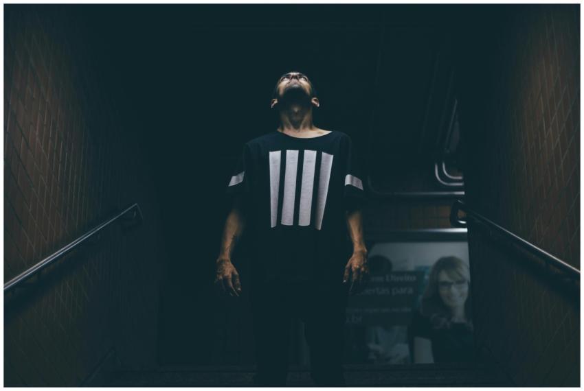 A young man stands in a dimly lit subway, looking