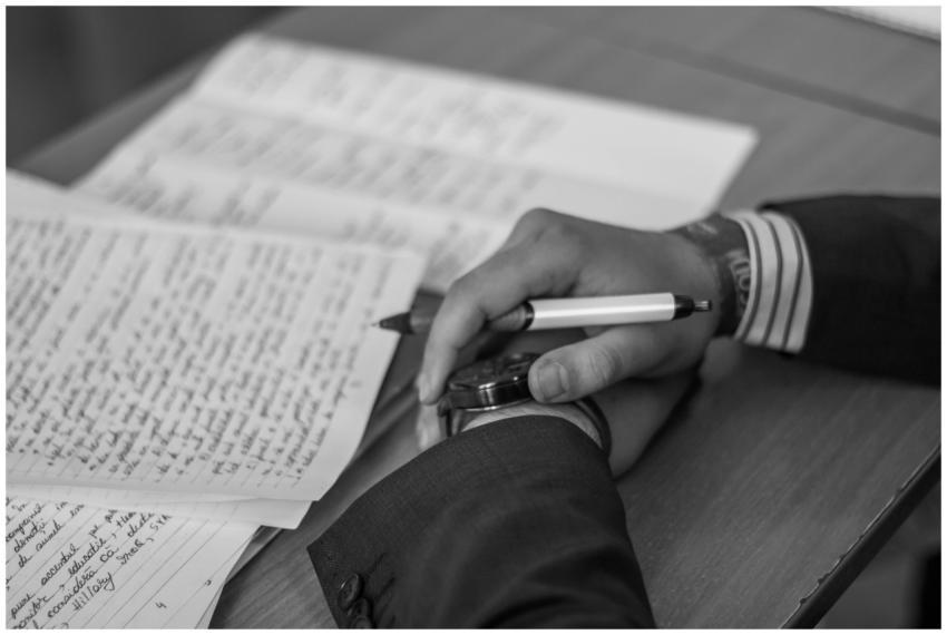 Close-up of a hand holding a pen over pages of wri