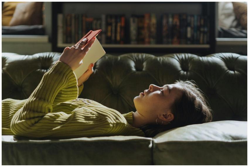 A young woman lies on a sofa reading a book, enjoy