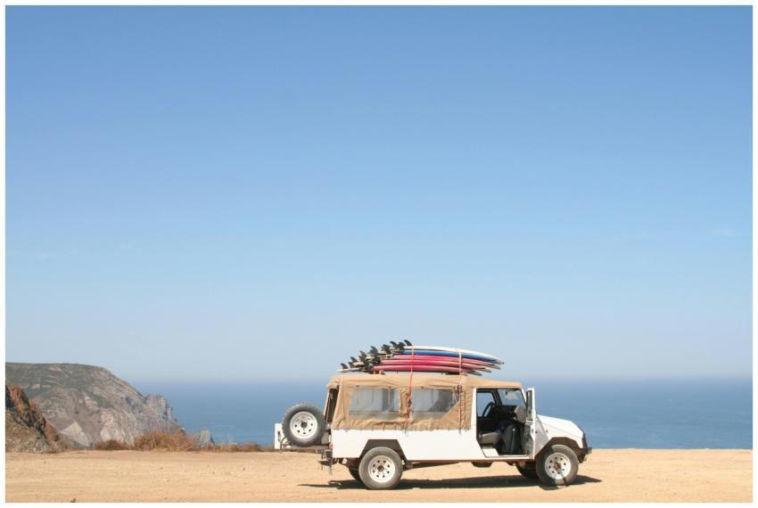 A jeep loaded with surfboards parked by a scenic o