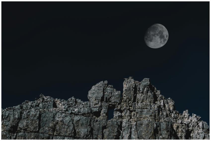 Scenic night view of a full moon rising above rock
