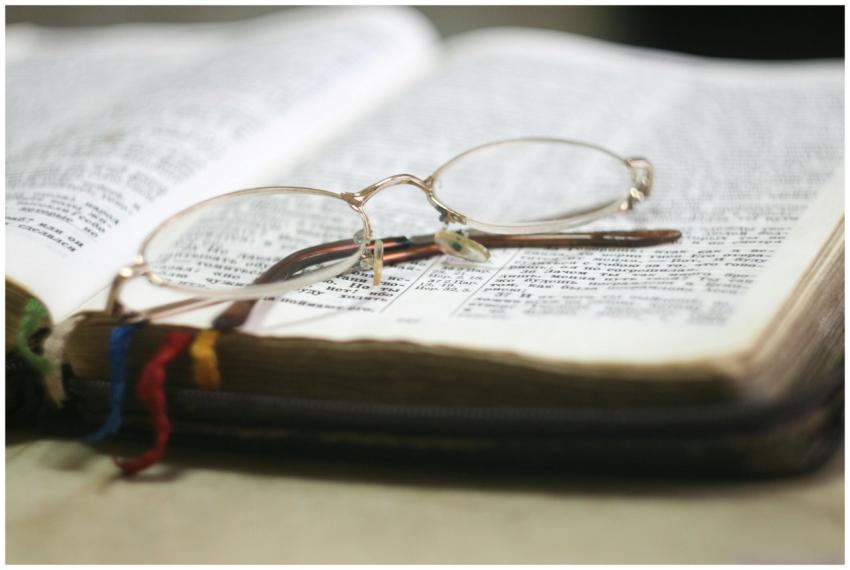 Close-up of eyeglasses atop an open Bible with col