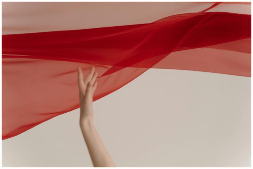 A delicate hand interacts with vibrant red fabric