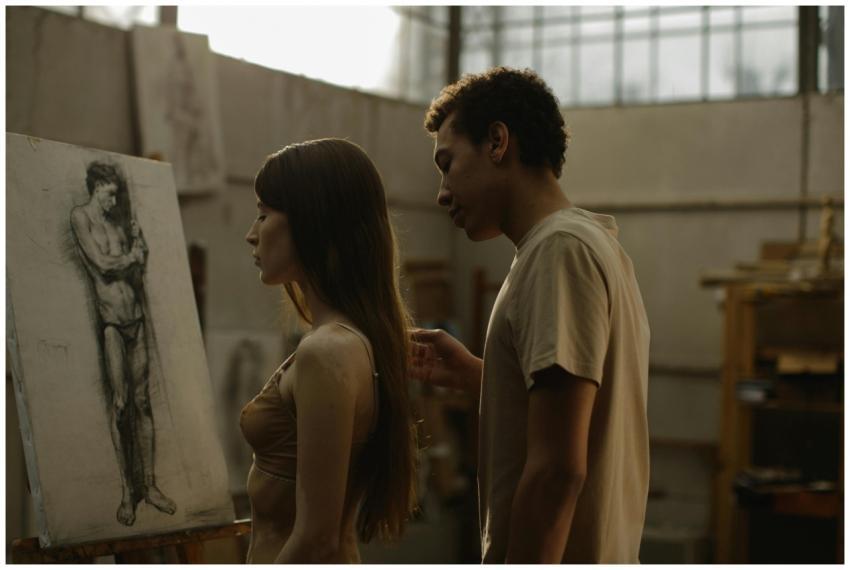 Artists in a studio focus on a nude sketch; soft l