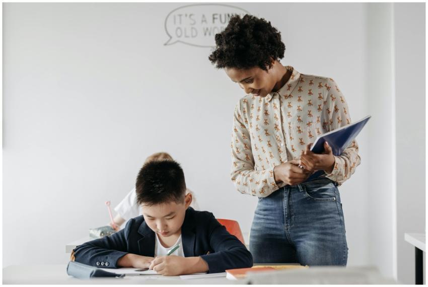 A teacher guides a student in a classroom, fosteri