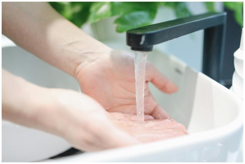 Hands washing under a modern bathroom faucet, emph