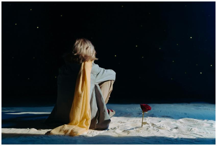 Adult sits with yellow scarf in sand under a starr