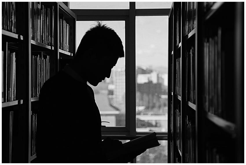 A moody silhouette of a man reading in a library,