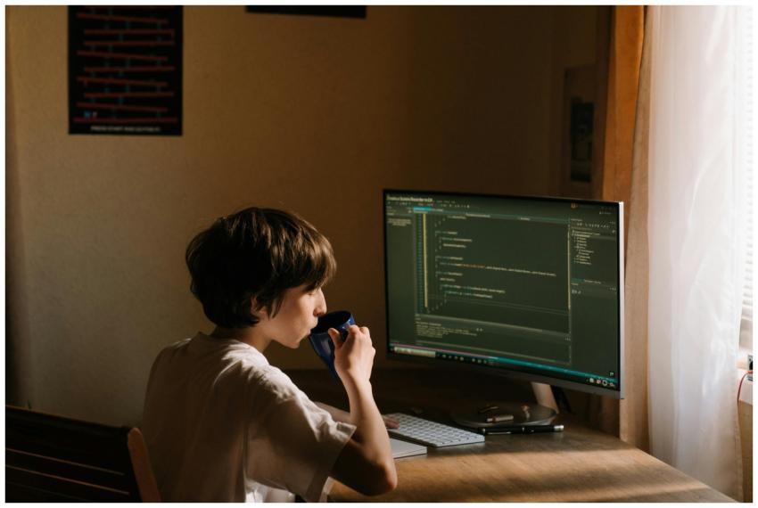 A young person coding at a desk with a computer an