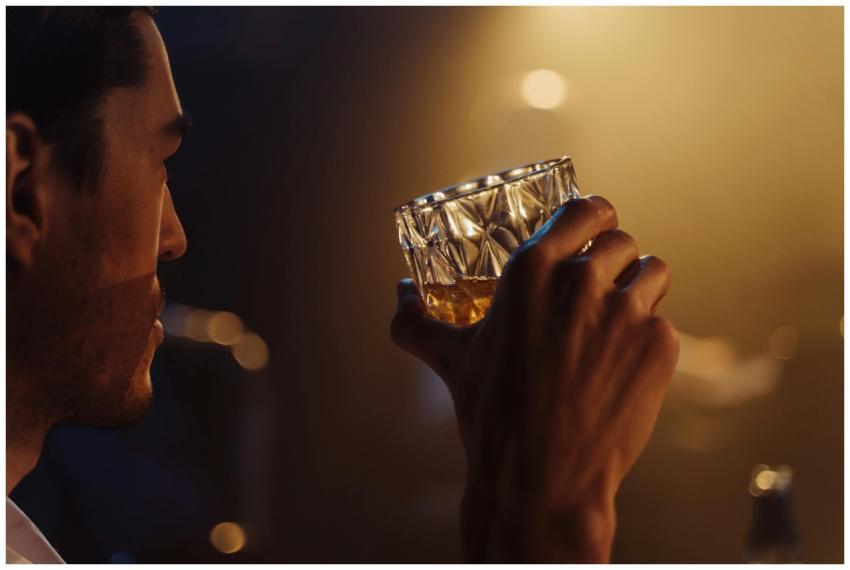 A man holding a whiskey glass in a dimly lit bar s