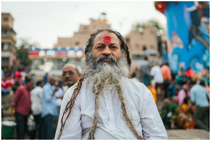 An elderly man with a red tilak standing in a busy