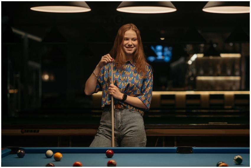 Smiling woman playing billiards indoors, holding c