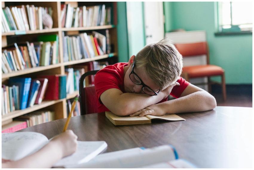 A young boy wearing glasses sleeps on a book in a
