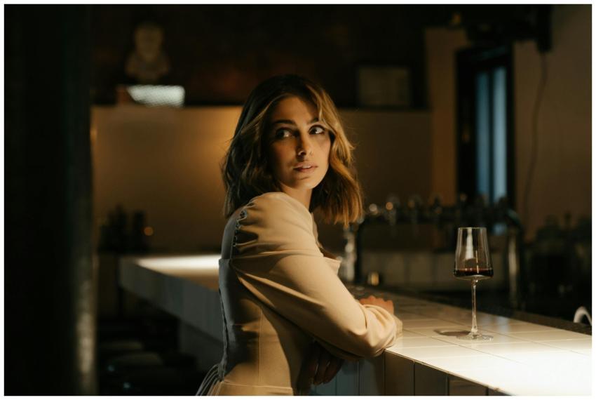 A glamorous woman in a stylish dress sits at a bar