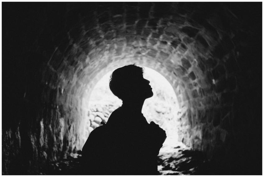Silhouetted person standing in a stone tunnel, cre