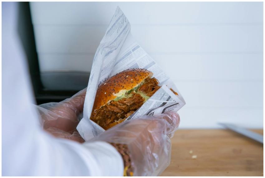Close-up of a gloved hand holding a pulled pork bu