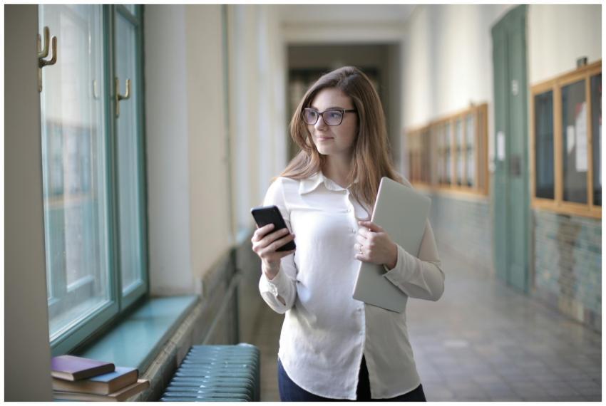 Female student with glasses holding a phone and la