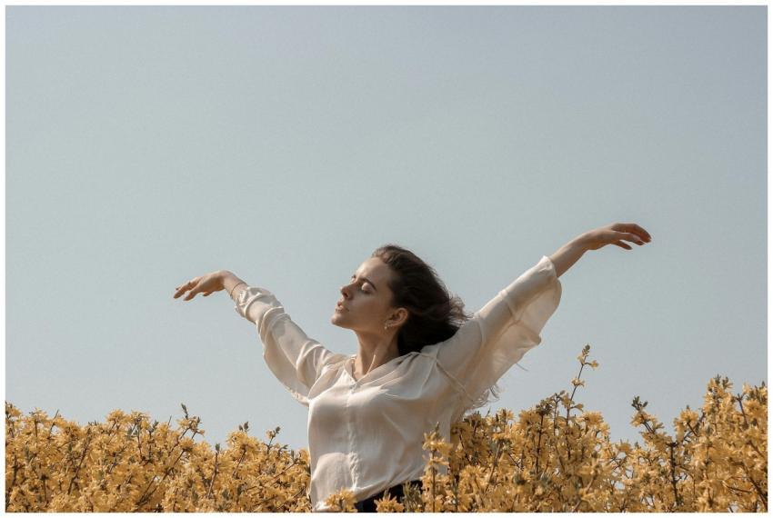 Woman with arms raised in a sunny field of yellow