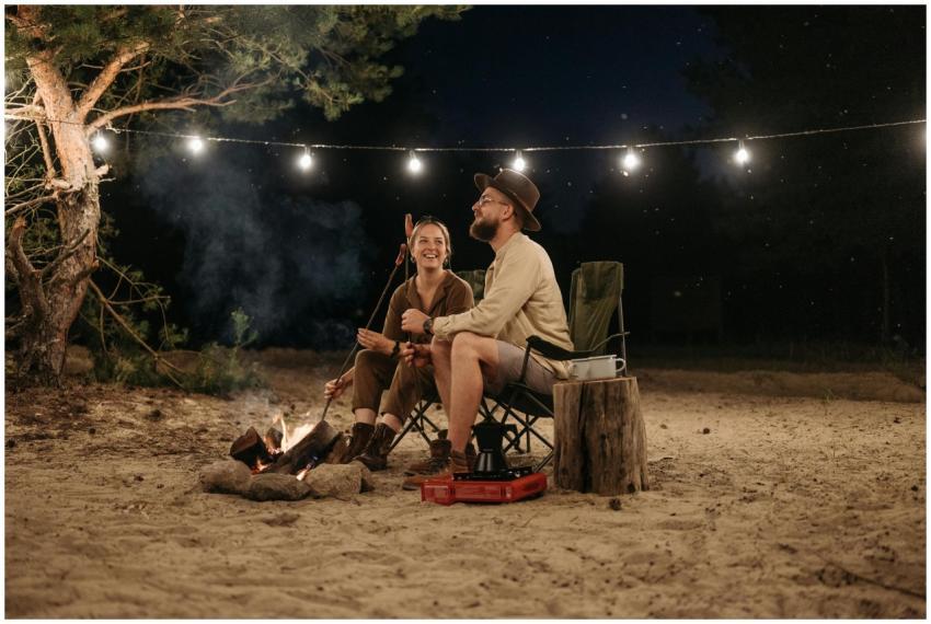 Happy couple sitting by a campfire, roasting sausa