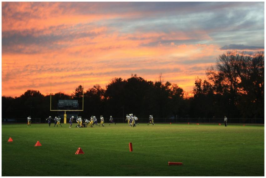 A vibrant sunset backdrop frames a football game o