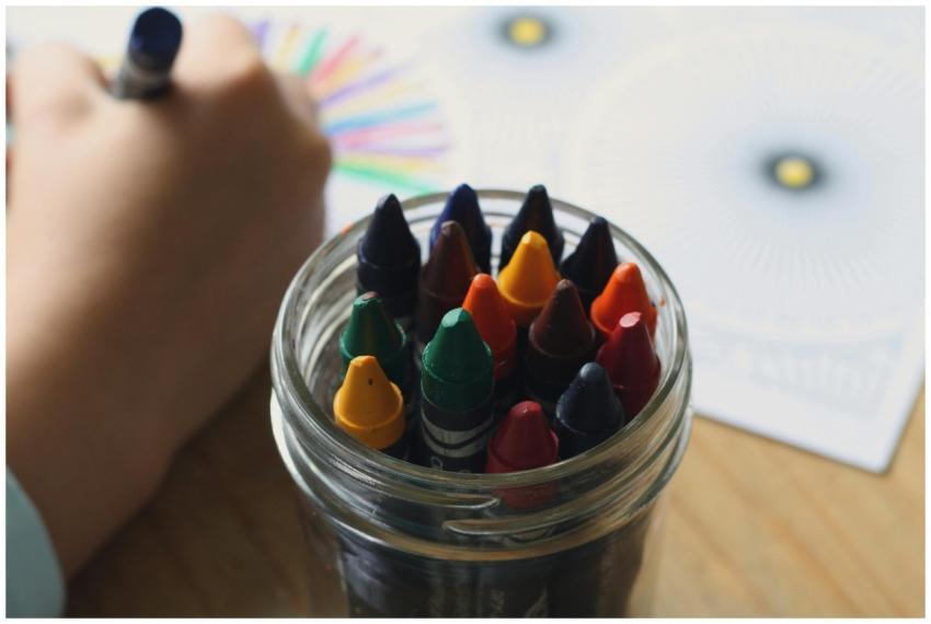 A child coloring with crayons in a jar, showcasing