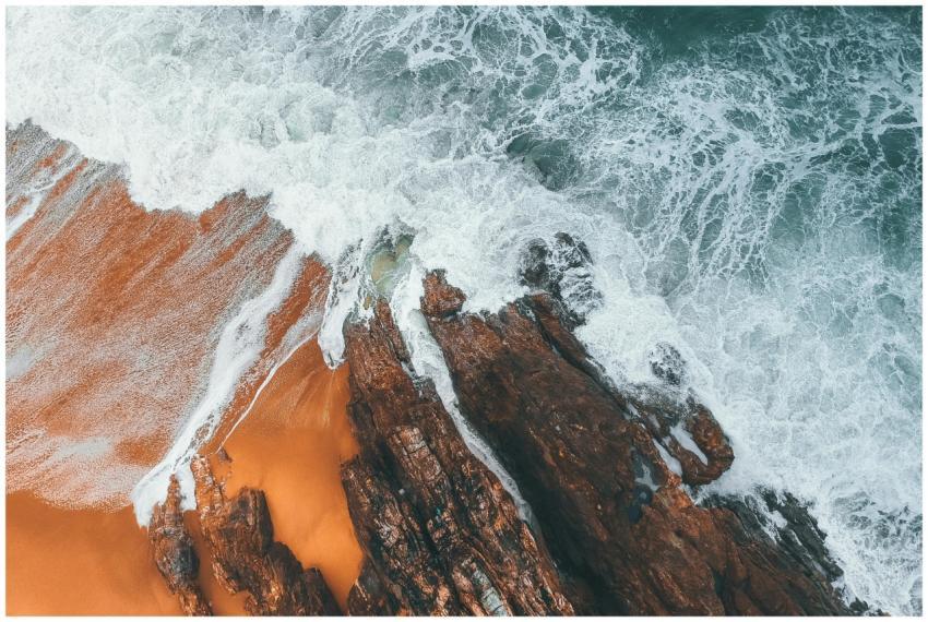 Drone shot capturing waves crashing onto a rocky c