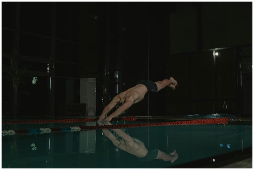 A male swimmer diving into an indoor pool, capture